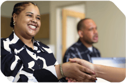 black woman smiling and shaking hands with an unseen recruiter; a black man is being interviewed in the background