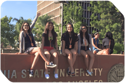four female students posing in front of a college entrance sign